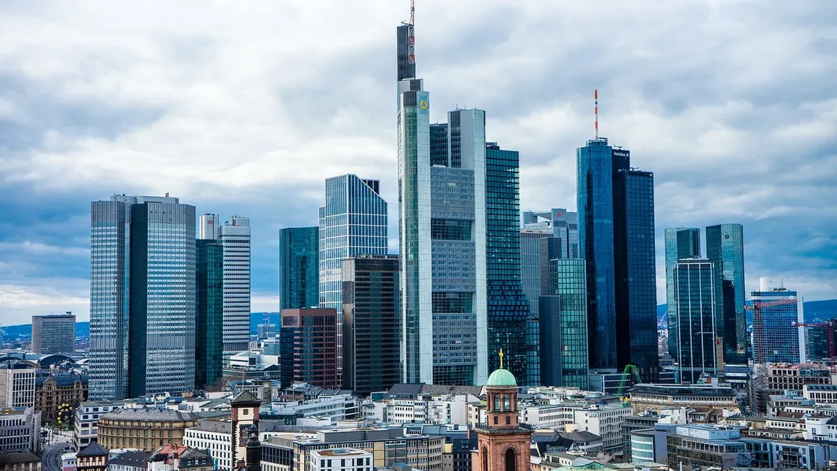 The skyline of Frankfurt, Germany, featuring a cluster of tall buildings, including the Commerzbank Tower, set against a cloudy sky.